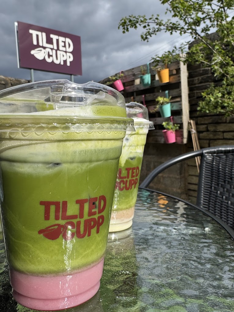 Two iced matcha drinks on a table outside under the Tilted Cupp sign